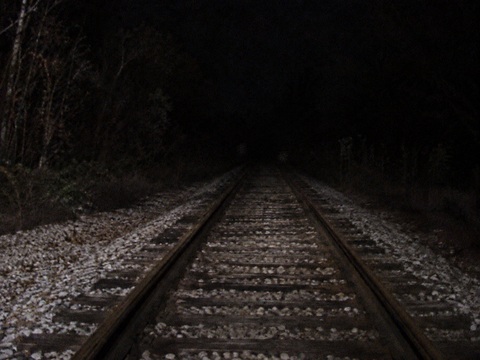 Night photograph looking north on NCS tracks from near Washington Street, available light only, high grain, something faintly visible between the rails in the middle distance